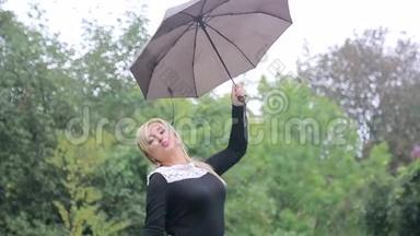 雨中带着雨伞的女人向公园里的照相机摆姿势。 穿着黑色礼服带伞的女孩